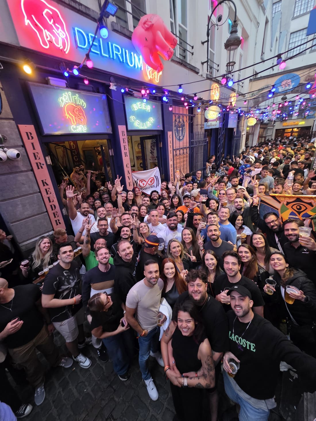 Encontro da família Never Ends lotando o beco do Delirium Café, em Bruxelas, com a bandeira da agência