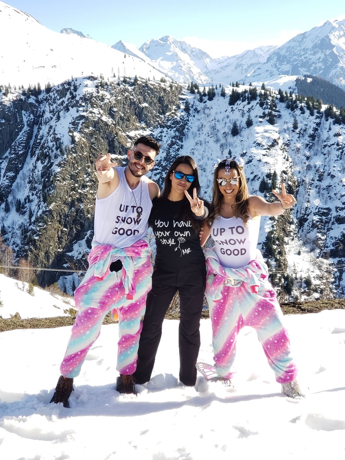 Três viajantes da Never Ends de macacão colorido na neve de Alpe d'Huez, com os Alpes franceses ao fundo, na viagem de 2020