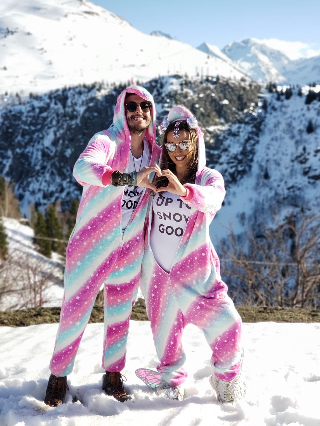 Casal do grupo da Never Ends fazendo coração com as mãos na neve de Alpe d'Huez, nos Alpes franceses