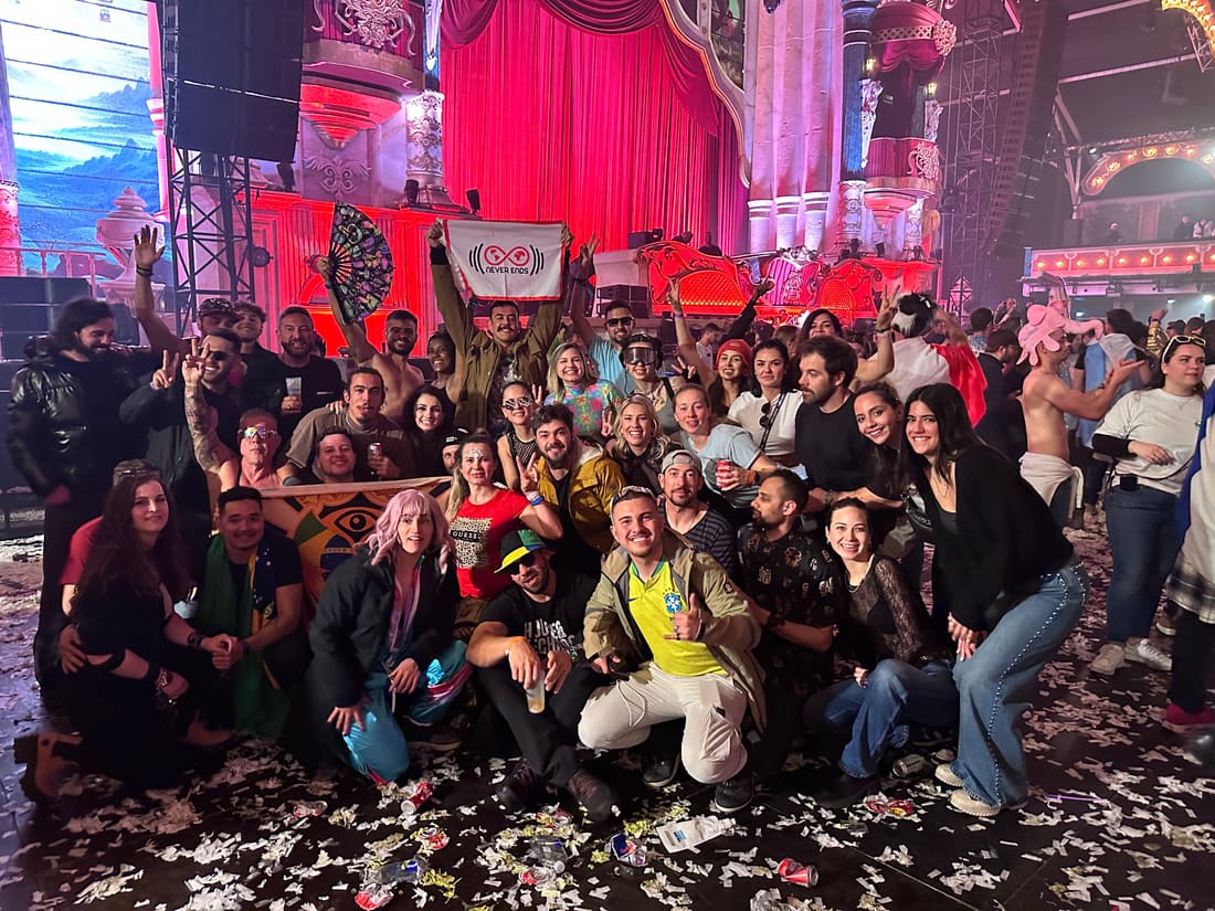 Grupo da Never Ends com a bandeira da agência levantada dentro do Mainstage coberto da Tomorrowland Winter, iluminado de vermelho