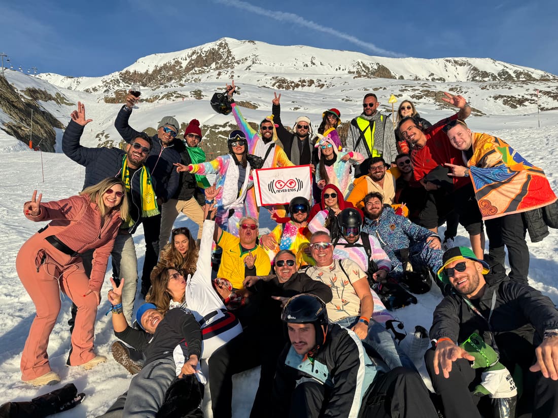 Grupo da Never Ends reunido na neve com a bandeira da agência, no fim de tarde em Alpe d'Huez