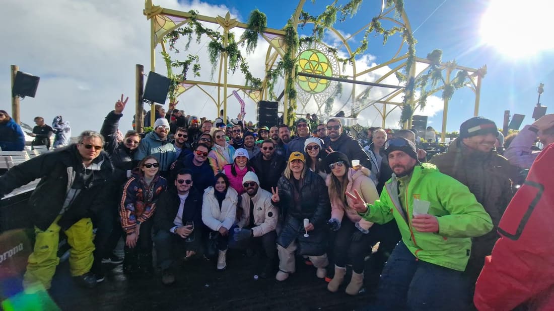 Grupo da Never Ends diante de um palco ao ar livre da Tomorrowland Winter, com a estrutura dourada e as flores do cenário