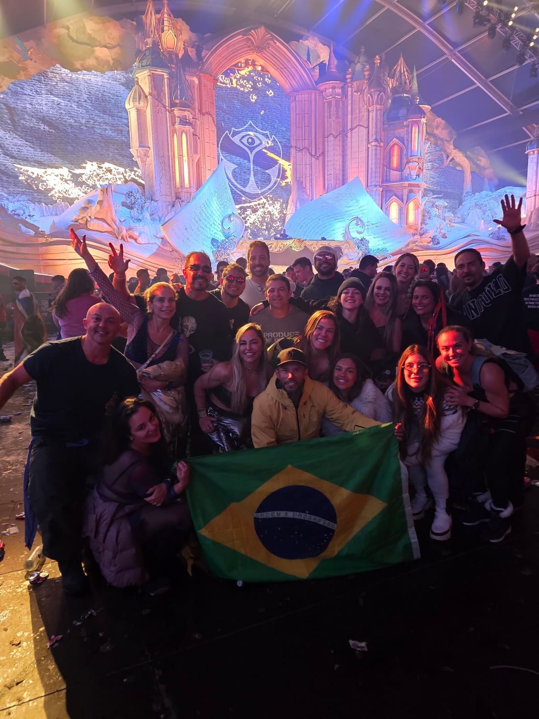 Grupo da Never Ends com a bandeira do Brasil diante do Mainstage coberto da Tomorrowland Winter, com o castelo de gelo iluminado e o símbolo do festival