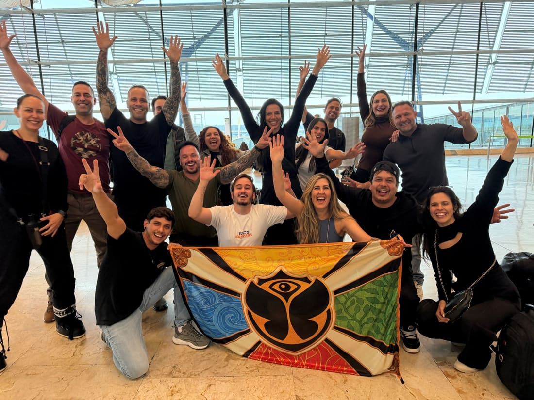 Grupo da Never Ends com a bandeira da Tomorrowland aberta no saguão do aeroporto, no começo da viagem pra Alpe d'Huez