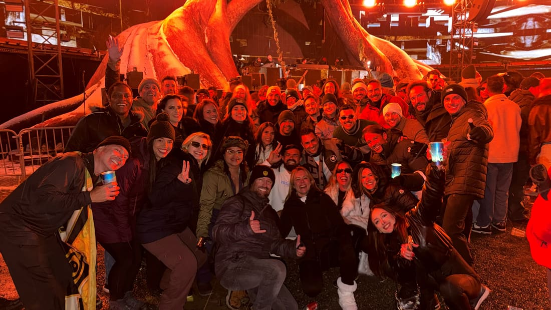 Grupo da Never Ends reunido diante de um palco da Tomorrowland Winter iluminado de laranja, à noite