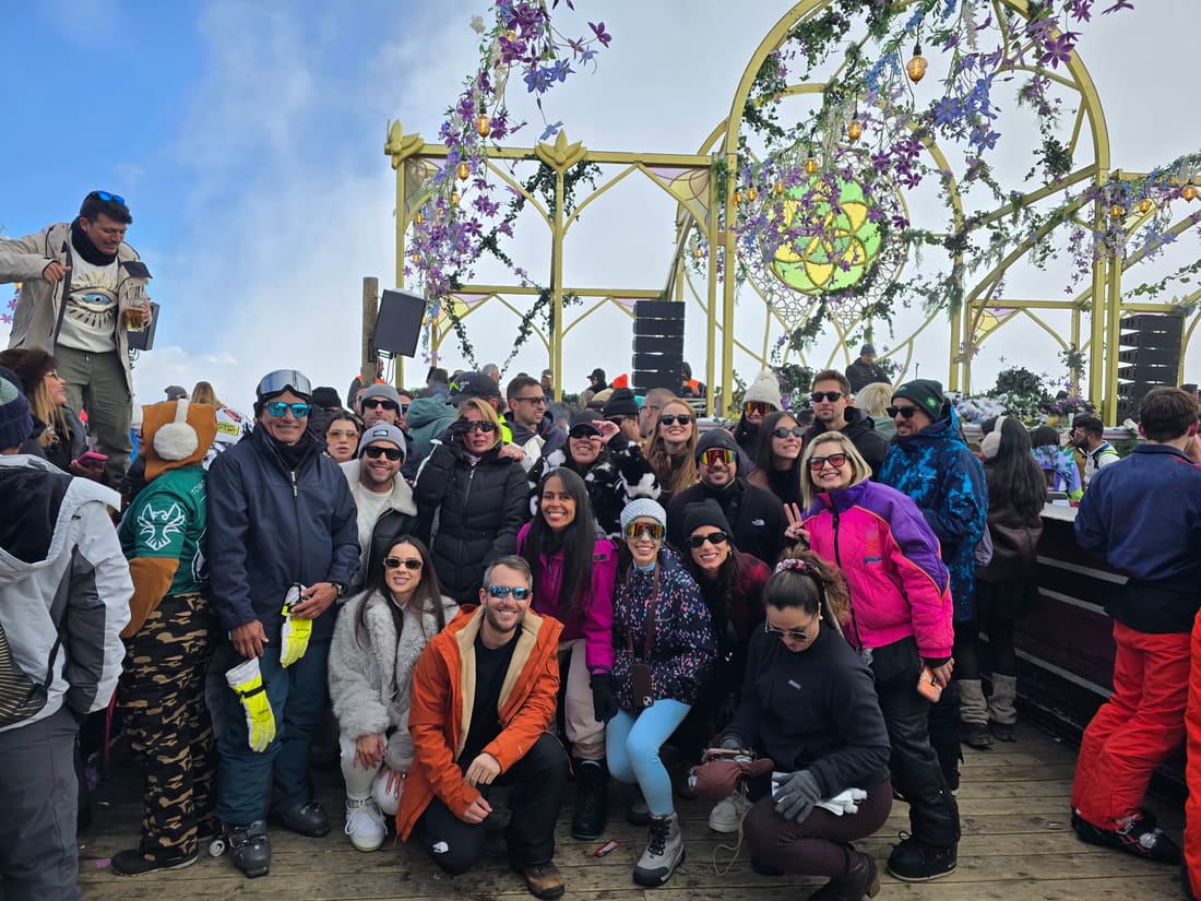 Grupo da Never Ends reunido no deque de um palco ao ar livre da Tomorrowland Winter, com a estrutura dourada e as flores do tema Sanctuary of the Butterflies