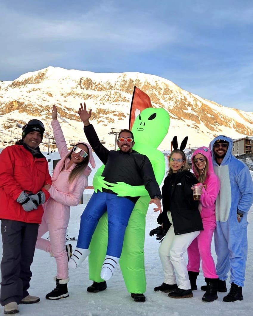 Viajantes da Never Ends de macacão na neve de Alpe d'Huez, com o pico dourado pelo sol do fim de tarde