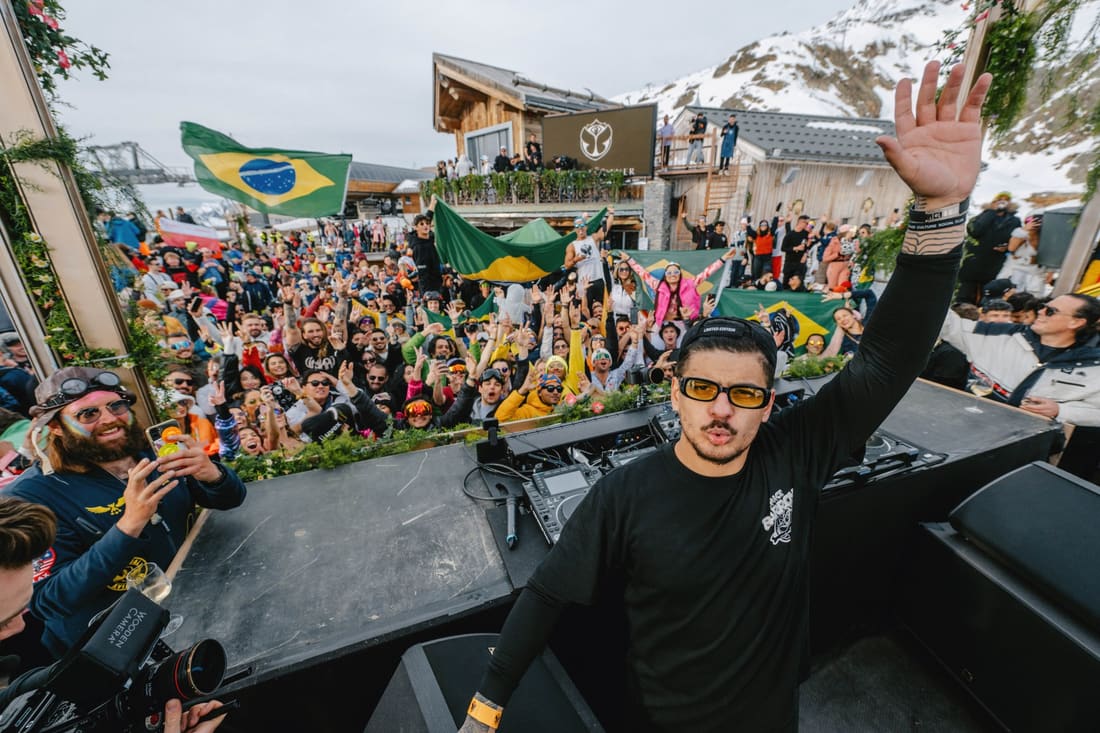 DJ acenando pro público brasileiro da Tomorrowland Winter, com várias bandeiras do Brasil abertas na multidão